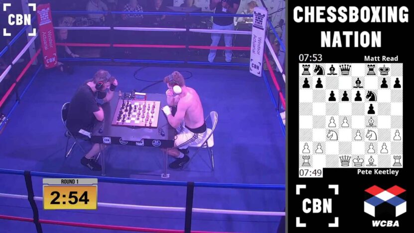 Two chessboxing competitors sit in a boxing ring playing chess while wearing headgear and gloves, with a live chessboard and timer displayed on screen