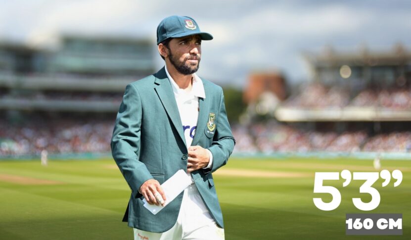 A Bangladeshi cricketer wearing a green blazer and cap stands on the cricket field, holding papers in hand